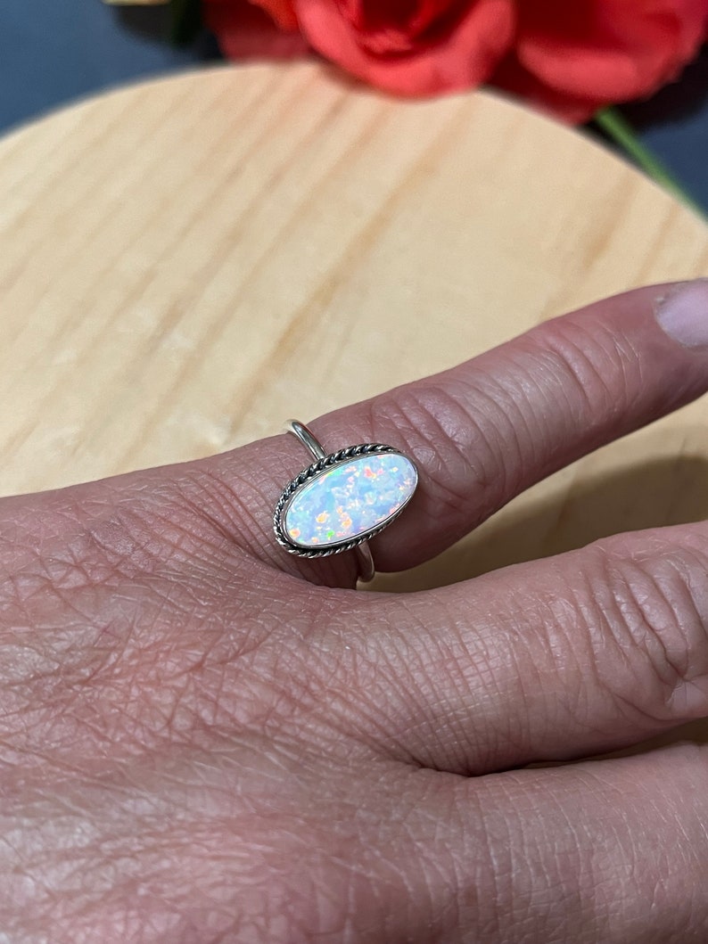 May include: A silver ring with an oval-shaped white opal gemstone. The ring has a delicate, twisted band.