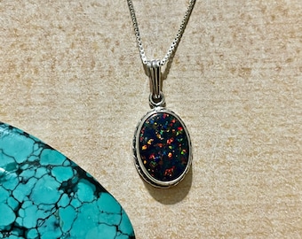 May include: A silver chain necklace with a black oval pendant featuring a colorful opal gemstone.