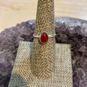 May include: A silver ring with a teardrop-shaped red carnelian gemstone.