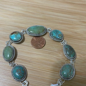 May include: Silver-toned bracelet featuring oval and teardrop-shaped turquoise stones. The stones are set in a decorative silver frame with a twisted rope design. The bracelet has a lobster clasp closure and an adjustable chain.