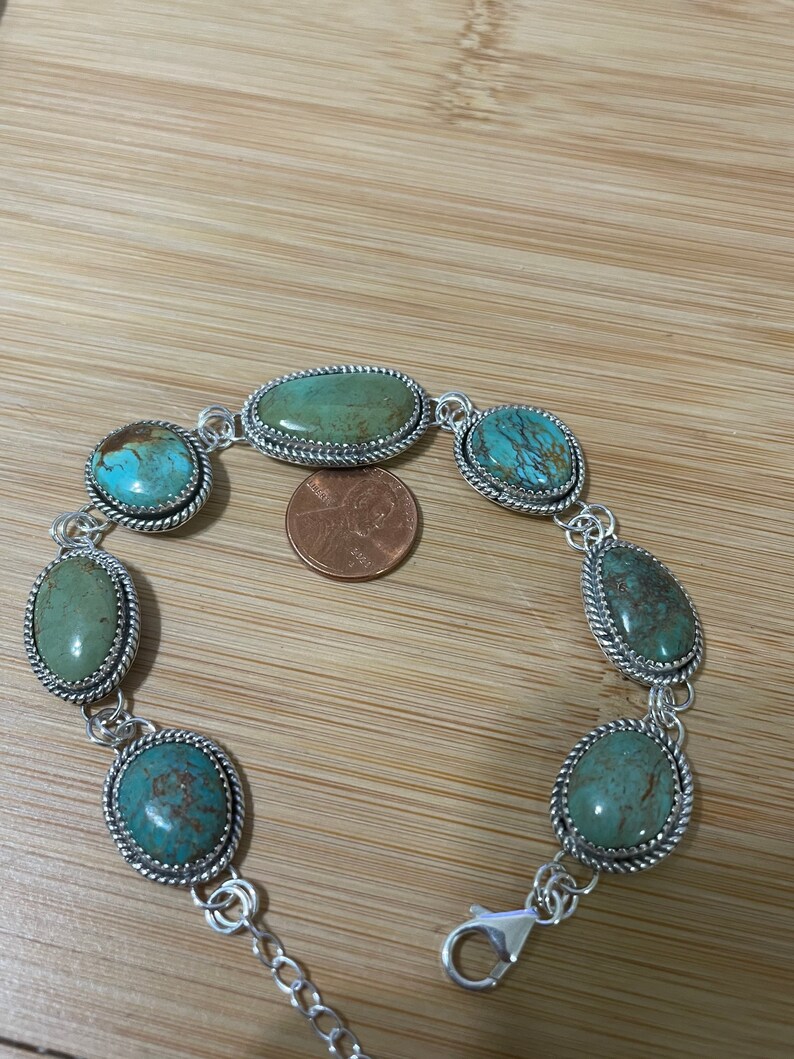 May include: Silver-toned bracelet featuring oval and teardrop-shaped turquoise stones. The stones are set in a decorative silver frame with a twisted rope design. The bracelet has a lobster clasp closure and an adjustable chain.
