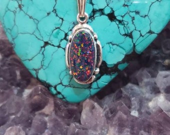 May include: A silver pendant with an oval-shaped opal gemstone. The opal is a dark purple with flashes of red, green, and blue.