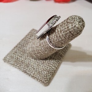 May include: A silver ring with a large, dark red gemstone set in a bezel setting. The ring is on a brown fabric ring display stand.