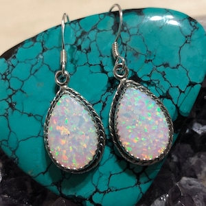 May include: A pair of silver dangle earrings with white opal teardrop stones. The earrings have a rope-like design around the edge of the stones.