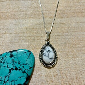 May include: A silver chain necklace with a white and black stone pendant. The pendant is set in a silver frame with a decorative border.