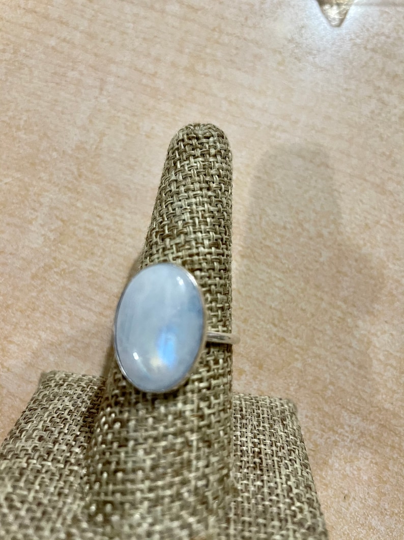 Puede incluir: Un anillo de plata con una gran piedra de luna ovalada. El anillo est&aacute; en un soporte de anillo de tela.