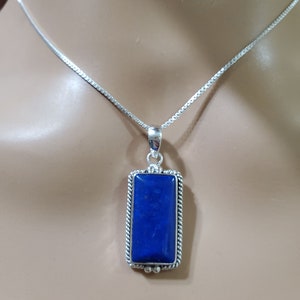 May include: A silver chain necklace with a rectangular pendant featuring a dark blue lapis lazuli stone.