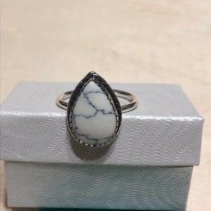 May include: A teardrop-shaped white howlite ring with a silver band and a black border around the stone.