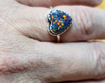May include: A silver ring with a heart-shaped opal gemstone. The opal is iridescent with shades of blue, green, and orange.