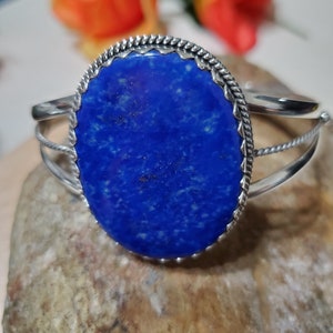 May include: A silver bracelet with a large oval lapis lazuli stone set in a silver bezel. The stone is a deep blue color with white veins and flecks.