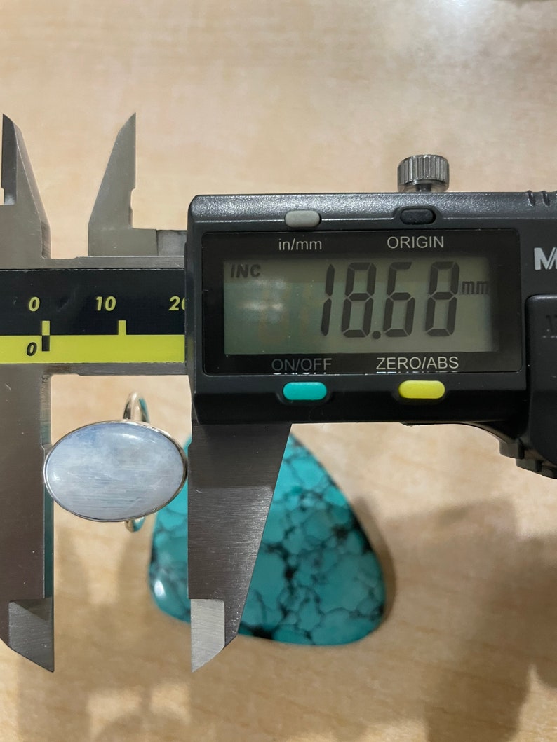 Puede incluir: Un anillo de plata con una piedra ovalada azul claro, medido a 18,68 mm, usando un calibre digital.