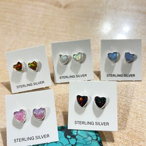 May include: Five pairs of sterling silver heart-shaped earrings with different colored opal stones. The earrings are displayed on white cards with the words "Sterling Silver" printed on them.