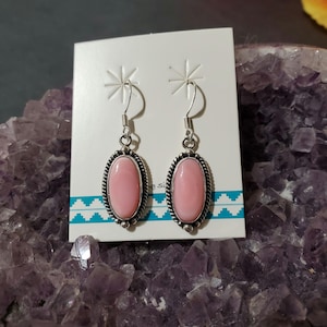 May include: A pair of silver earrings with pink oval stones set in a silver bezel. The earrings have a simple design and are perfect for everyday wear.