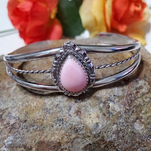 May include: A silver bracelet with a pink stone set in a decorative silver bezel. The bracelet has a twisted wire design.