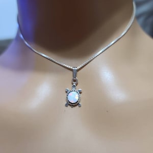 May include: A silver chain necklace with a small turtle pendant featuring a white opal stone.