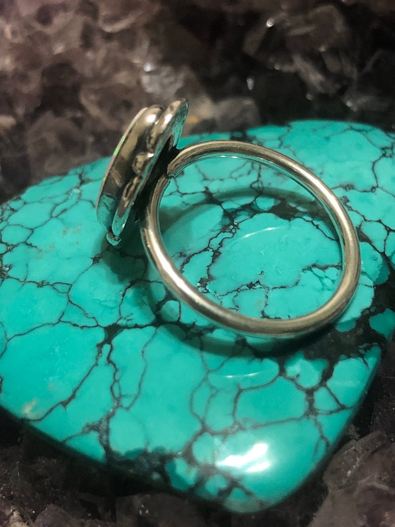 May include: A silver ring with a white opal gemstone set in a bezel setting. The ring is on a turquoise background.