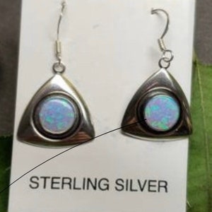 May include: A pair of sterling silver earrings with a triangular shape and a round opal stone in the center. The earrings are displayed on a white card with the text "STERLING SILVER".