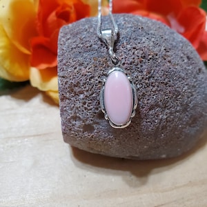 May include: A silver chain necklace with a pink oval pendant. The pendant is set in a silver frame with a decorative design.