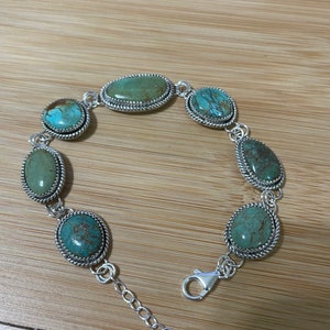 May include: A silver bracelet featuring oval and round turquoise stones. The stones are set in a silver frame with a twisted rope design. The bracelet has a lobster clasp closure and an adjustable chain.