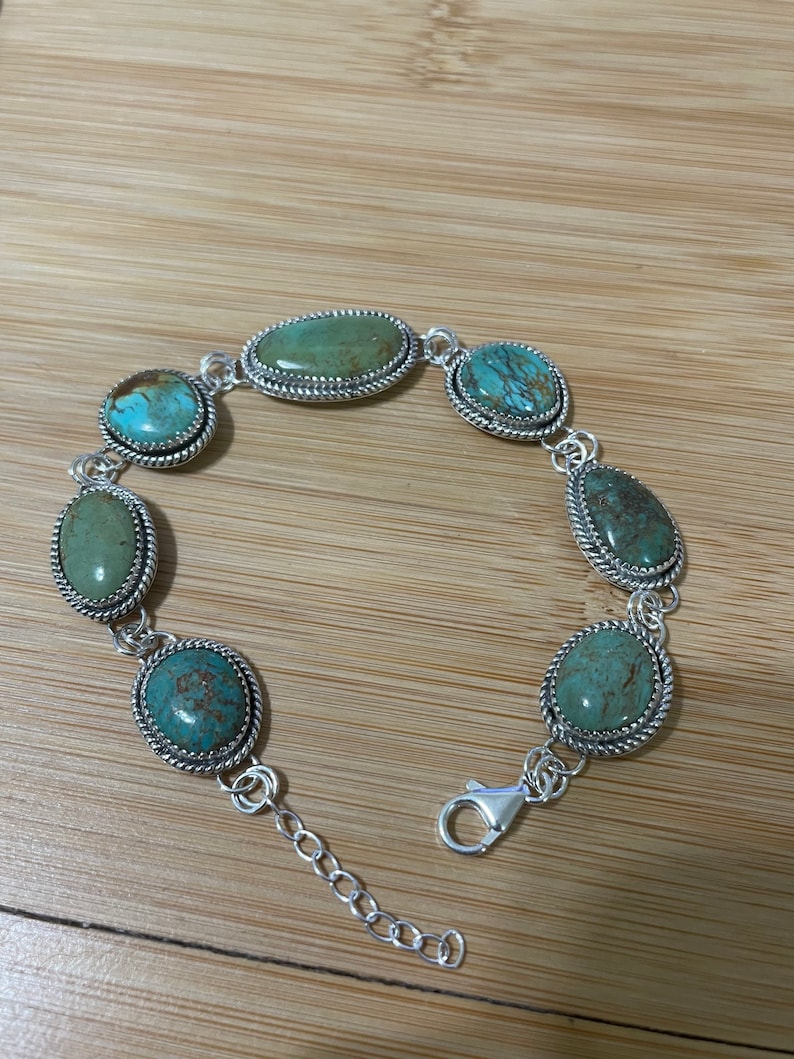 May include: A silver bracelet featuring oval and round turquoise stones. The stones are set in a silver frame with a twisted rope design. The bracelet has a lobster clasp closure and an adjustable chain.