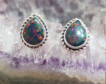 May include: A pair of silver teardrop earrings with black opal stones. The earrings have a rope-like design around the edges of the stones.