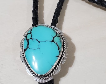 May include: A turquoise bolo tie with a silver setting and a black leather cord.