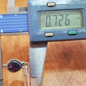 May include: A black opal pendant with a silver chain. The opal is a teardrop shape and measures 0.726 inches in length.
