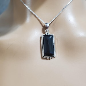 May include: A silver chain necklace with a black rectangular pendant. The pendant has a silver border and a black gemstone in the center.