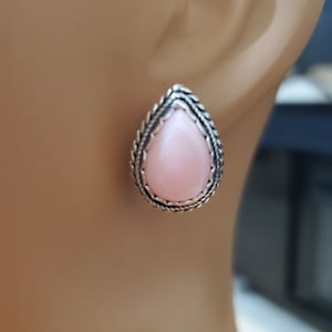 May include: A pair of silver earrings with a pink teardrop-shaped stone set in a detailed silver frame.