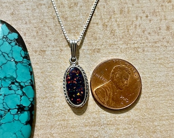 May include: A silver chain necklace with a pendant featuring a dark red, black, and orange opal stone set in a silver oval frame. The pendant is about the size of a US penny.