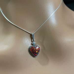 May include: A silver chain necklace with a heart-shaped pendant featuring a red and orange opal gemstone.