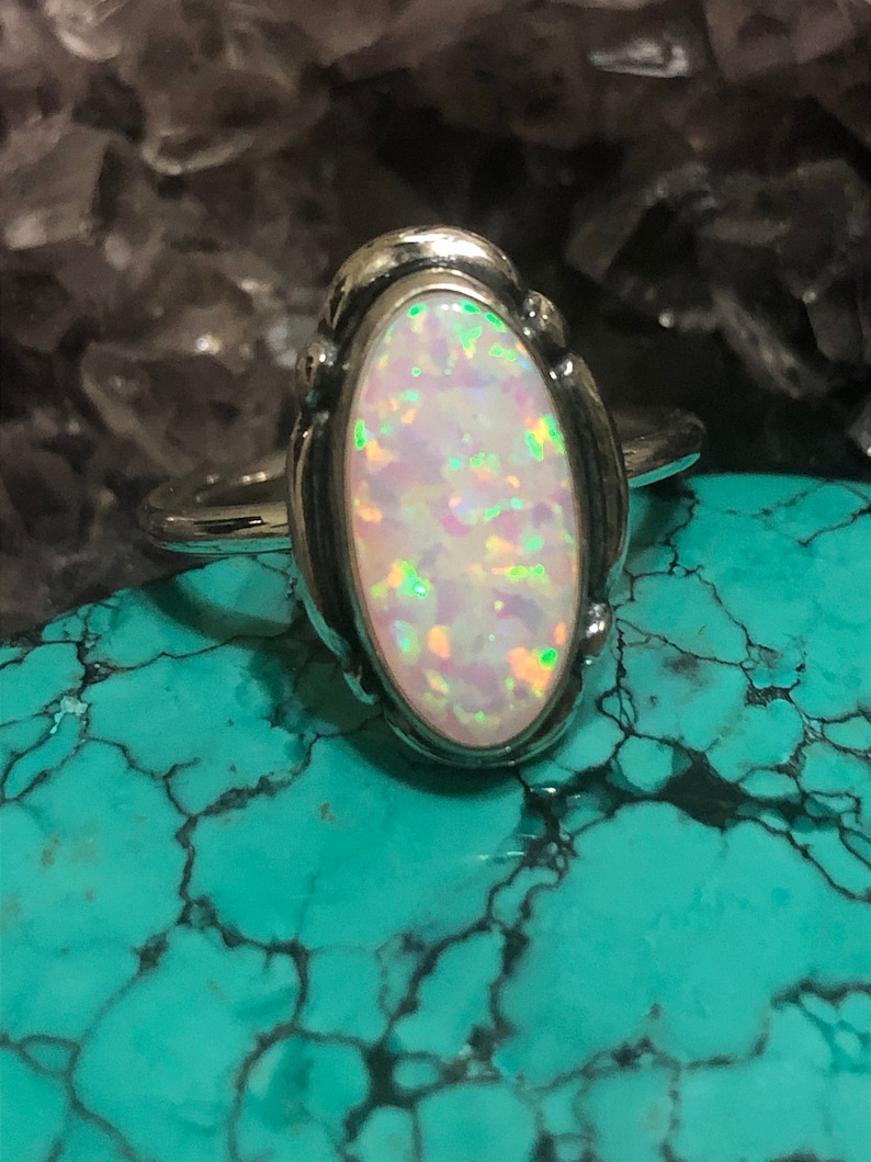 May include: A silver ring with an oval-shaped opal gemstone. The opal is a pale pink color with green and blue iridescence.