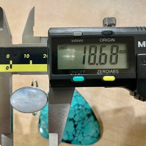 Puede incluir: Primer plano de un calibre digital que mide un anillo de piedra ovalado de color azul claro. El calibre indica 18,68 mm.