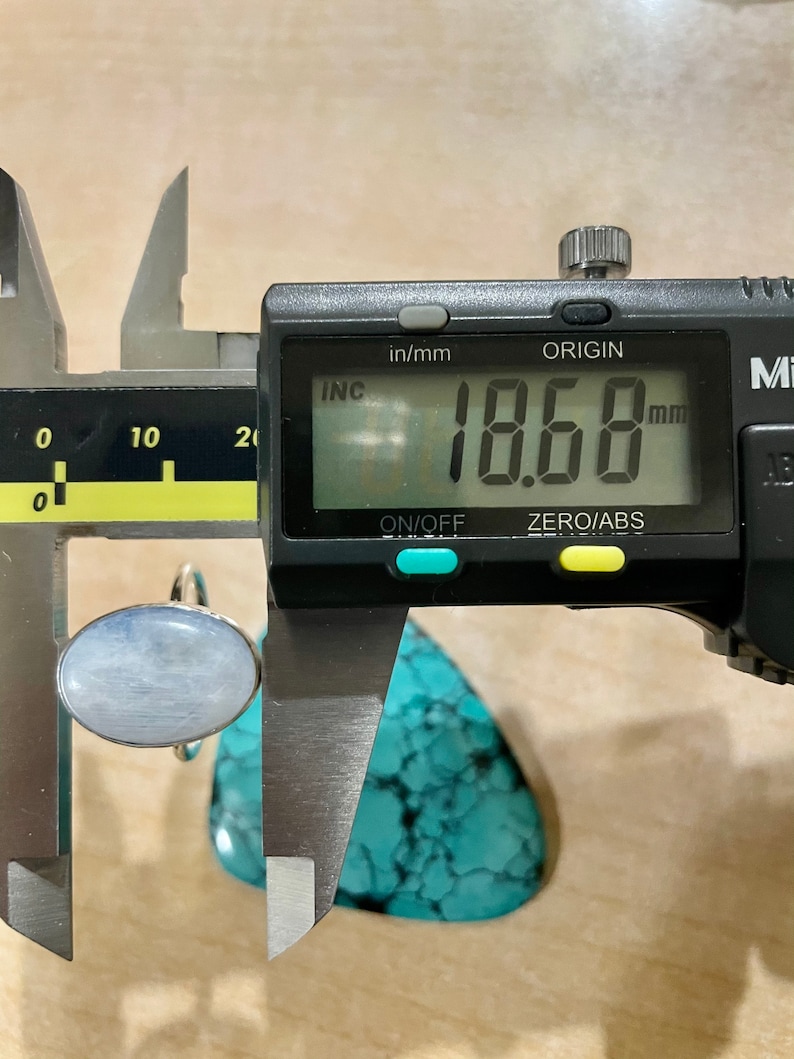 Puede incluir: Primer plano de un calibre digital que mide un anillo de piedra ovalado de color azul claro. El calibre indica 18,68 mm.