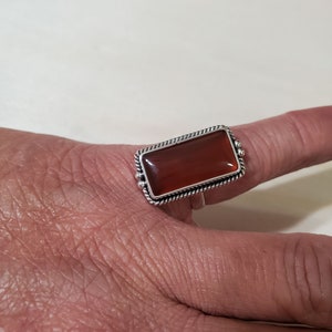 May include: A silver ring with a rectangular carnelian stone set in a twisted wire bezel.