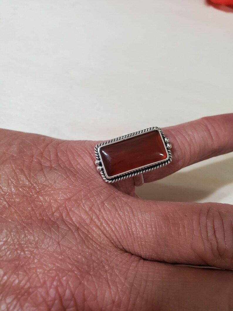 May include: A silver ring with a rectangular carnelian stone set in a twisted wire bezel.
