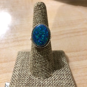 May include: A silver ring with a blue and green opal gemstone set in a silver bezel. The ring is on a ring display stand.
