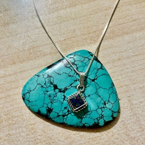 May include: A silver chain necklace with a square pendant featuring a dark blue and iridescent opal stone set in a silver frame.
