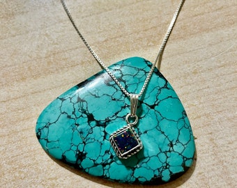 May include: A silver chain necklace with a square pendant featuring a dark blue and iridescent opal stone set in a silver frame.