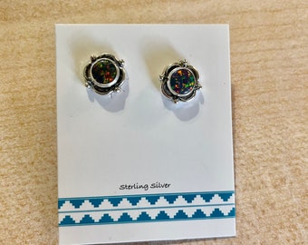 May include: A pair of sterling silver stud earrings with a floral design. Each earring features a dark, oval-shaped stone with iridescent colors. The earrings are displayed on a white card with the text "Sterling Silver" and a turquoise geometric border.