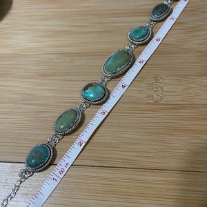 May include: A silver bracelet featuring oval turquoise stones. The bracelet is approximately 7 inches long. Each stone is set in a silver bezel with a twisted rope design. The bracelet is displayed on a wooden surface.