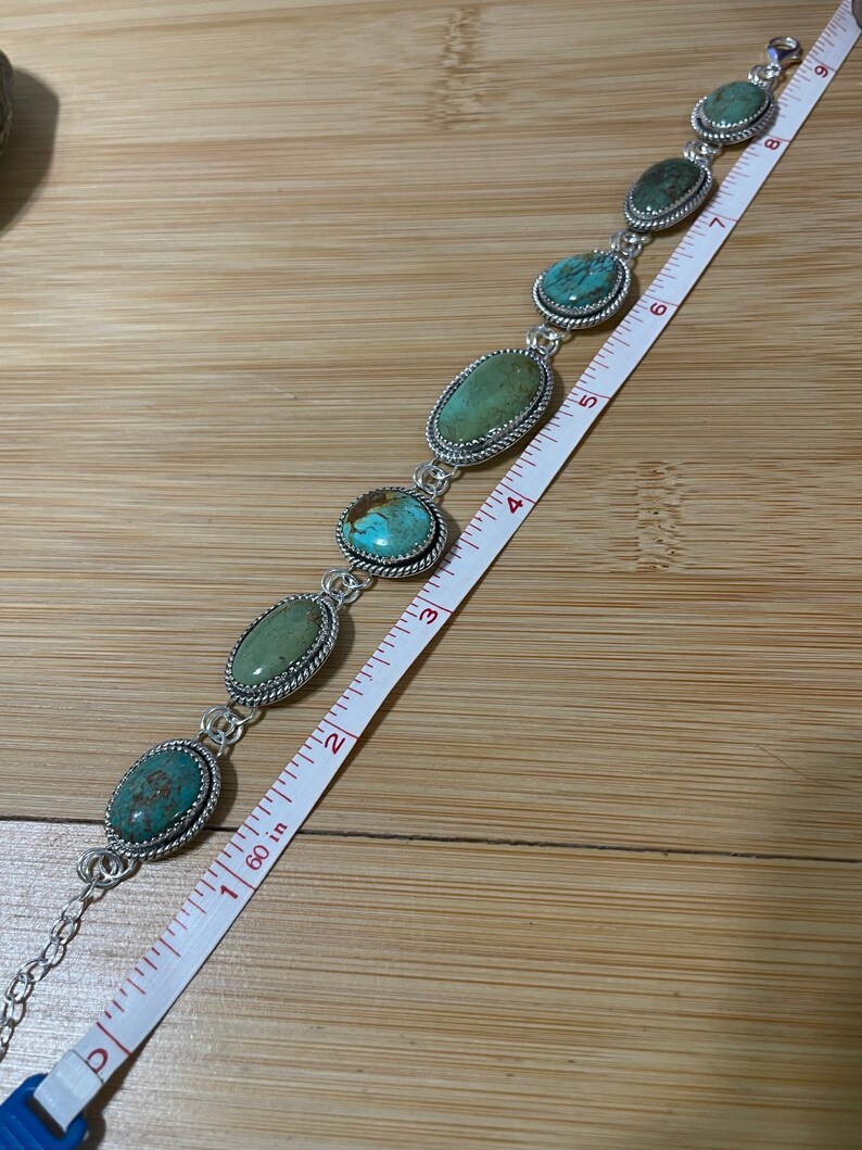 May include: A silver bracelet featuring oval turquoise stones. The bracelet is approximately 7 inches long. Each stone is set in a silver bezel with a twisted rope design. The bracelet is displayed on a wooden surface.