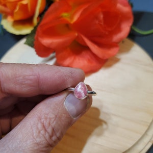 Puede incluir: Un anillo de plata con una piedra preciosa rosa en forma de l&aacute;grima. El anillo est&aacute; en un dedo.
