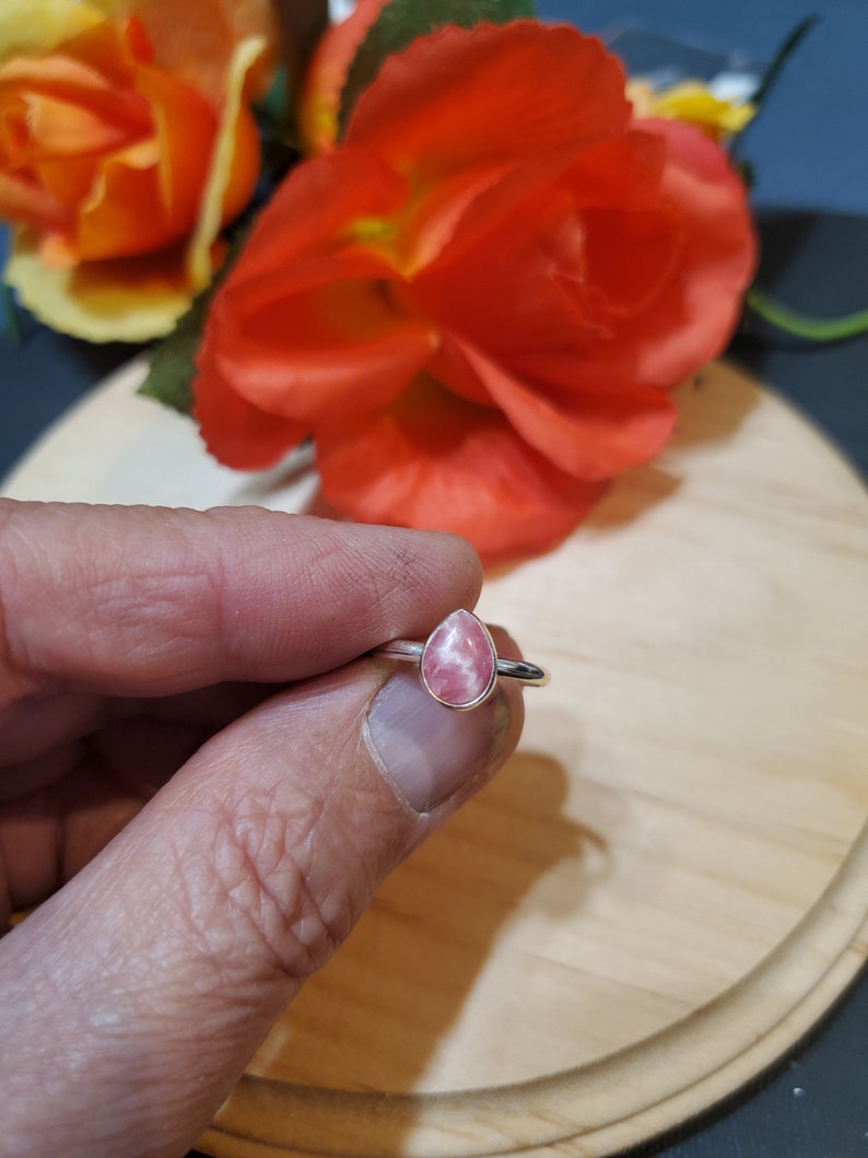 Puede incluir: Un anillo de plata con una piedra preciosa rosa en forma de l&aacute;grima. El anillo est&aacute; en un dedo.