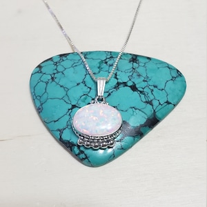 May include: A silver chain necklace with a white opal pendant. The pendant is oval shaped and has a silver beaded border.