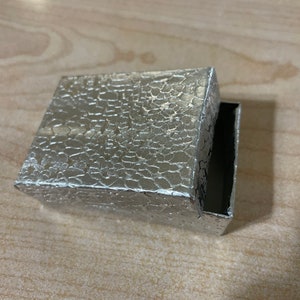 May include: A silver box with a textured, embossed surface. The box is open and the inside is black.