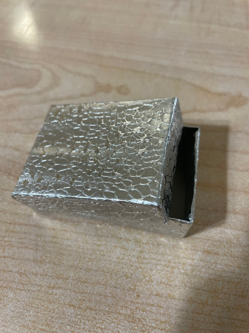 May include: A silver box with a textured, embossed surface. The box is open and the inside is black.