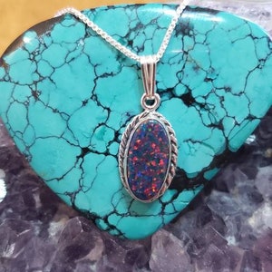 May include: A silver chain necklace with a pendant featuring a dark oval opal set in a silver bezel. The opal has a rainbow of colors, including red, blue, and green.