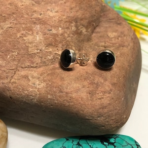 May include: A pair of silver stud earrings with black round gemstones. The earrings are on a brown rock.