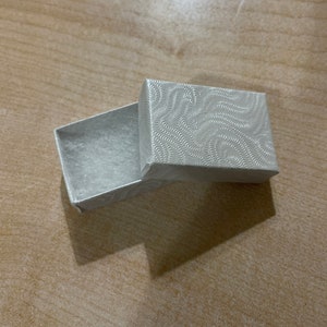 May include: A small, white, rectangular box with a textured, swirling pattern on the lid. The box is open and empty.